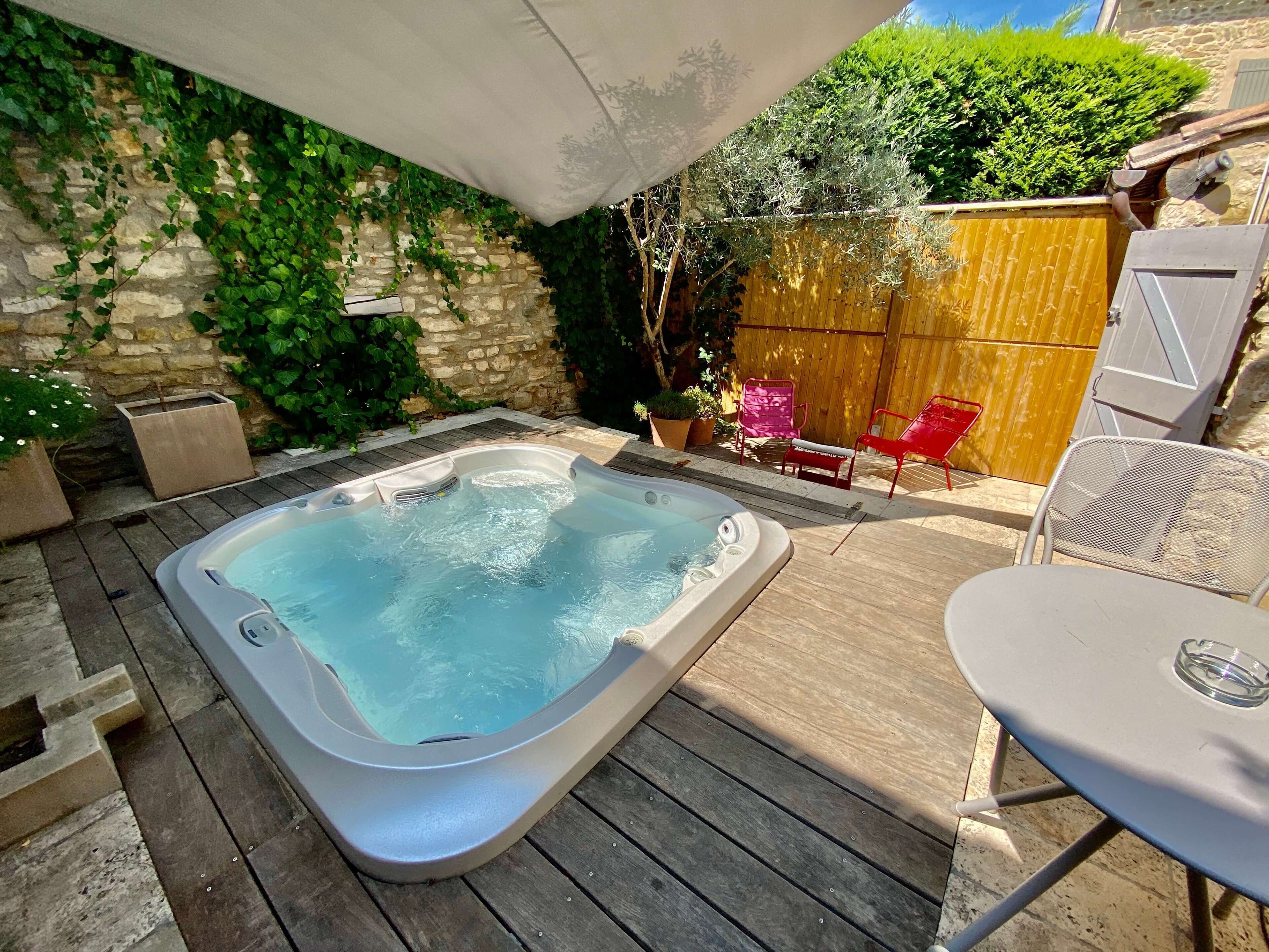 A hot tub on a wooden deck with a stone wall and greenery in the background.