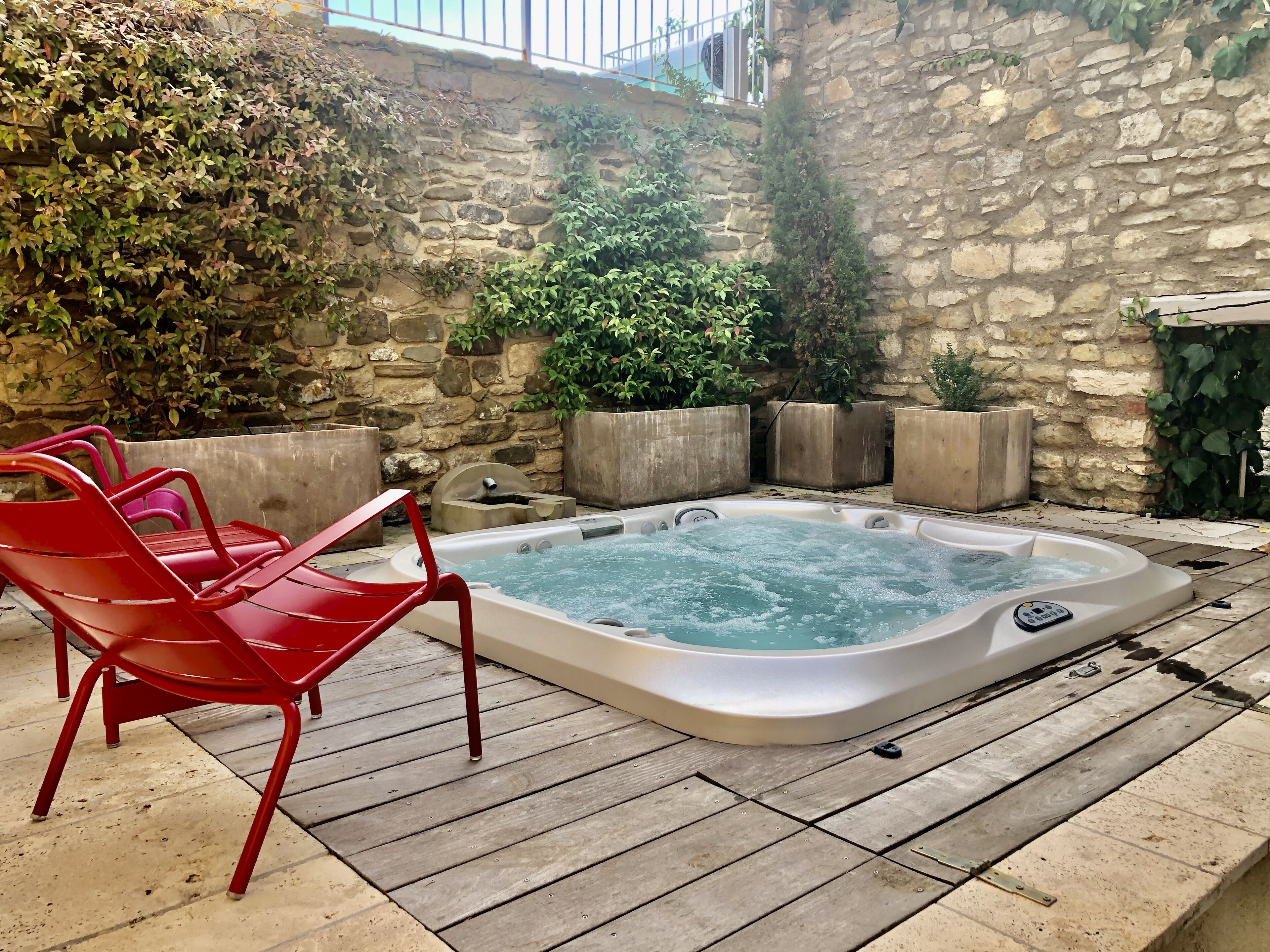 Un jacuzzi con sillas rojas, rodeado de muros de piedra y follaje.