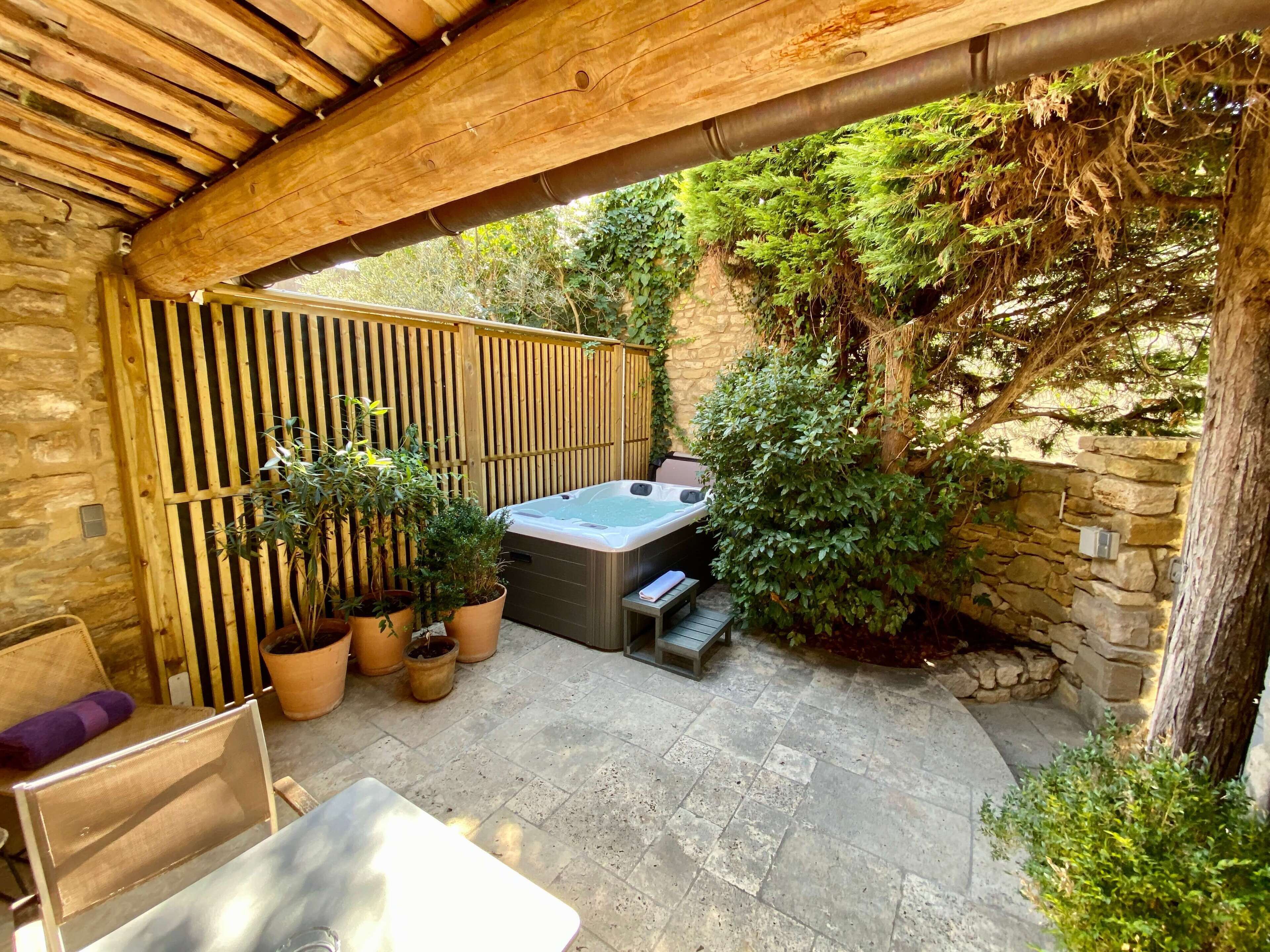Un patio techado con jacuzzi, plantas en macetas y paredes de piedra.