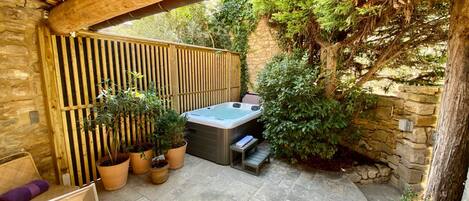 Un patio techado con jacuzzi, plantas en macetas y paredes de piedra.
