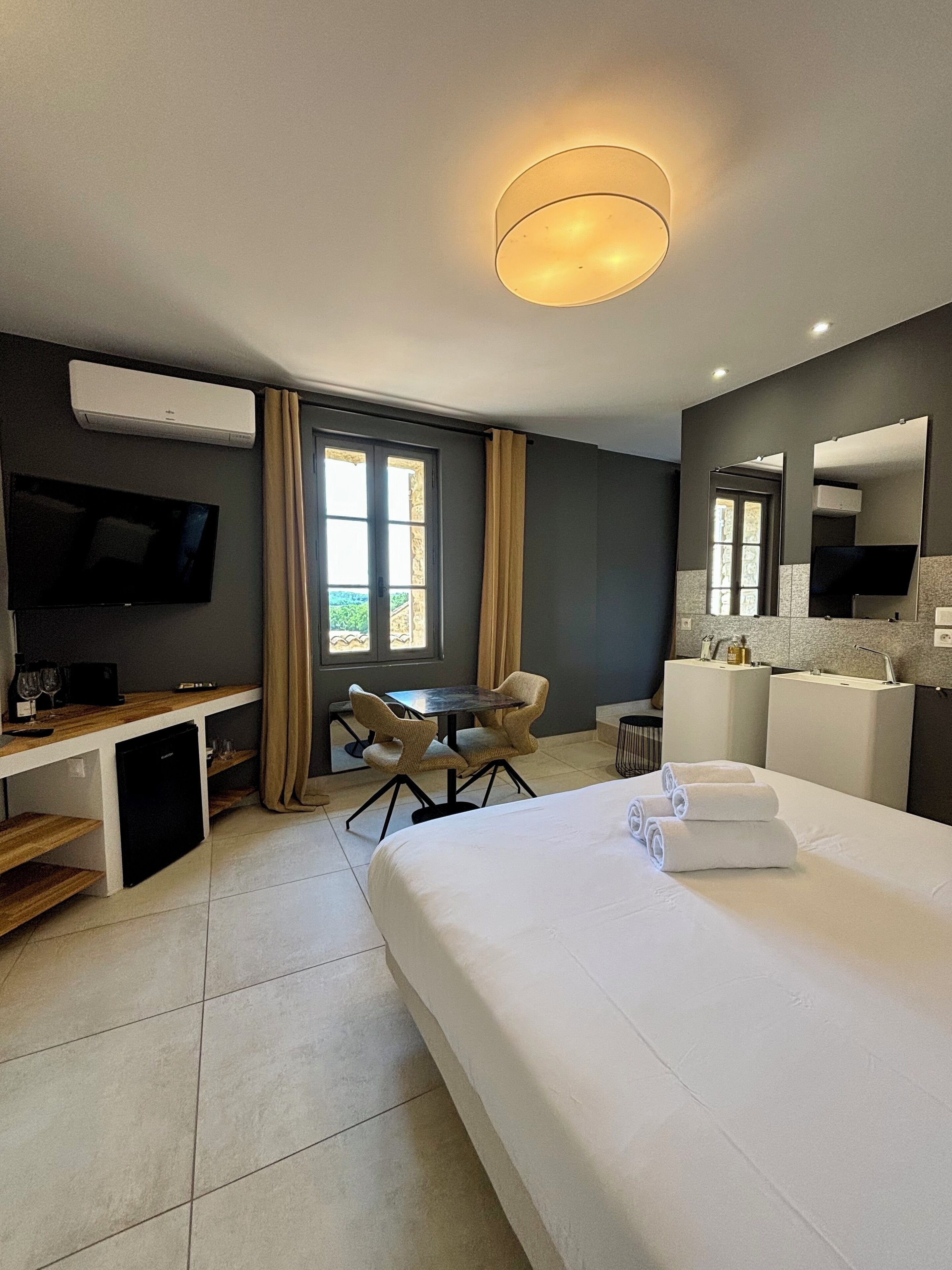 A modern hotel room with a bed, desk, TV, and a window with curtains.