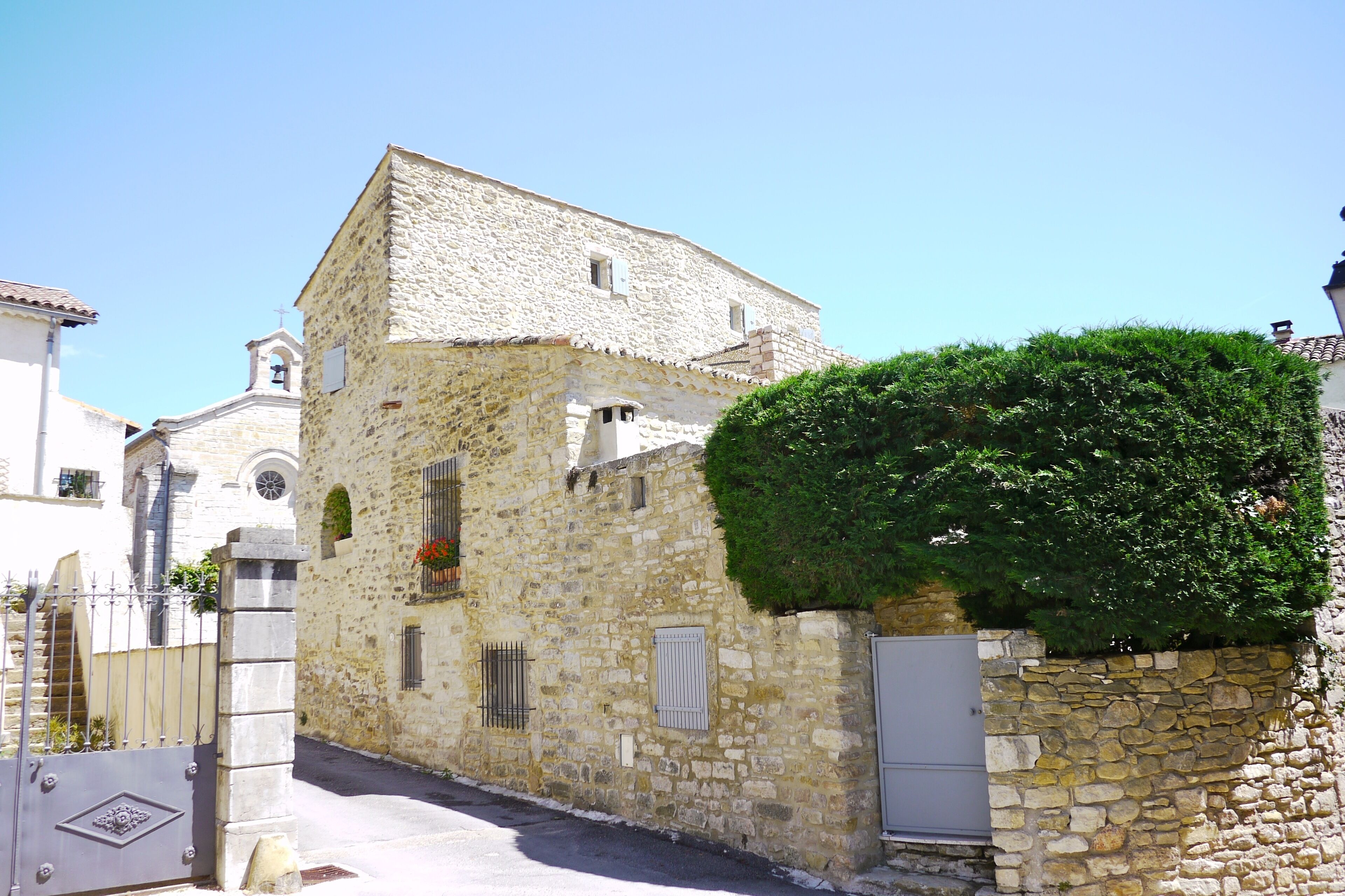 A stone building with a bell tower, a gate, and a hedge.