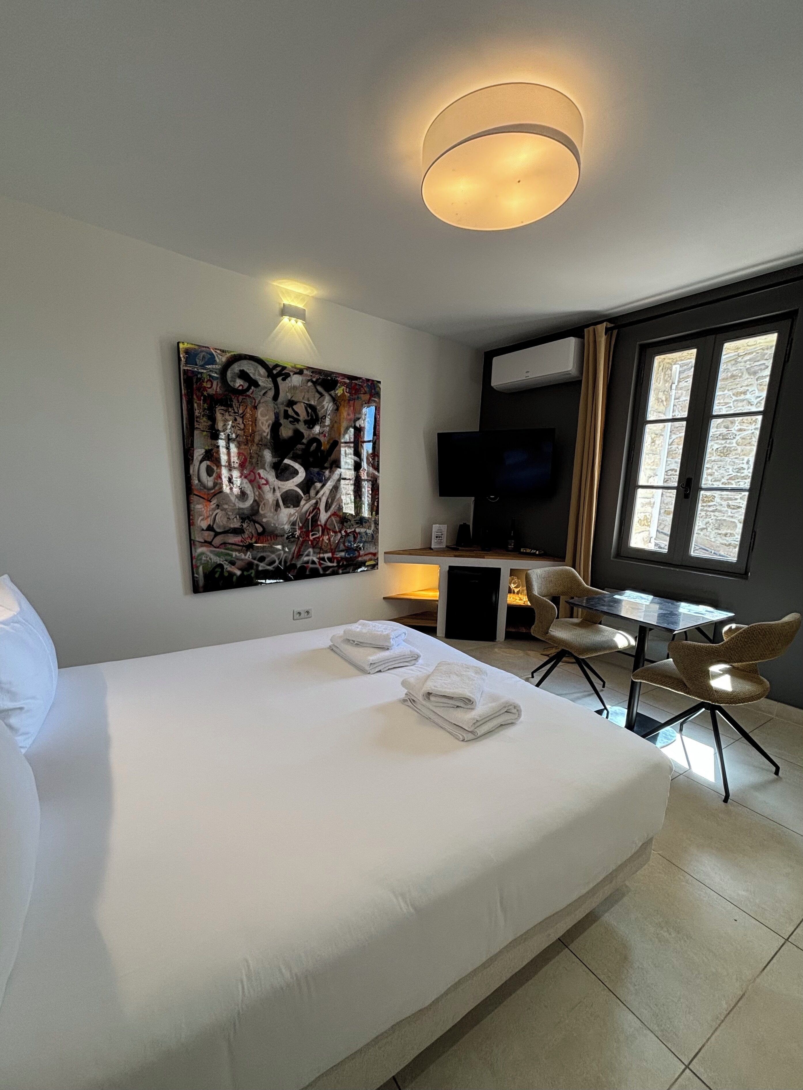 Une chambre d’hôtel avec un grand lit, un bureau avec une chaise, un téléviseur à écran plat et une fenêtre avec des rideaux.