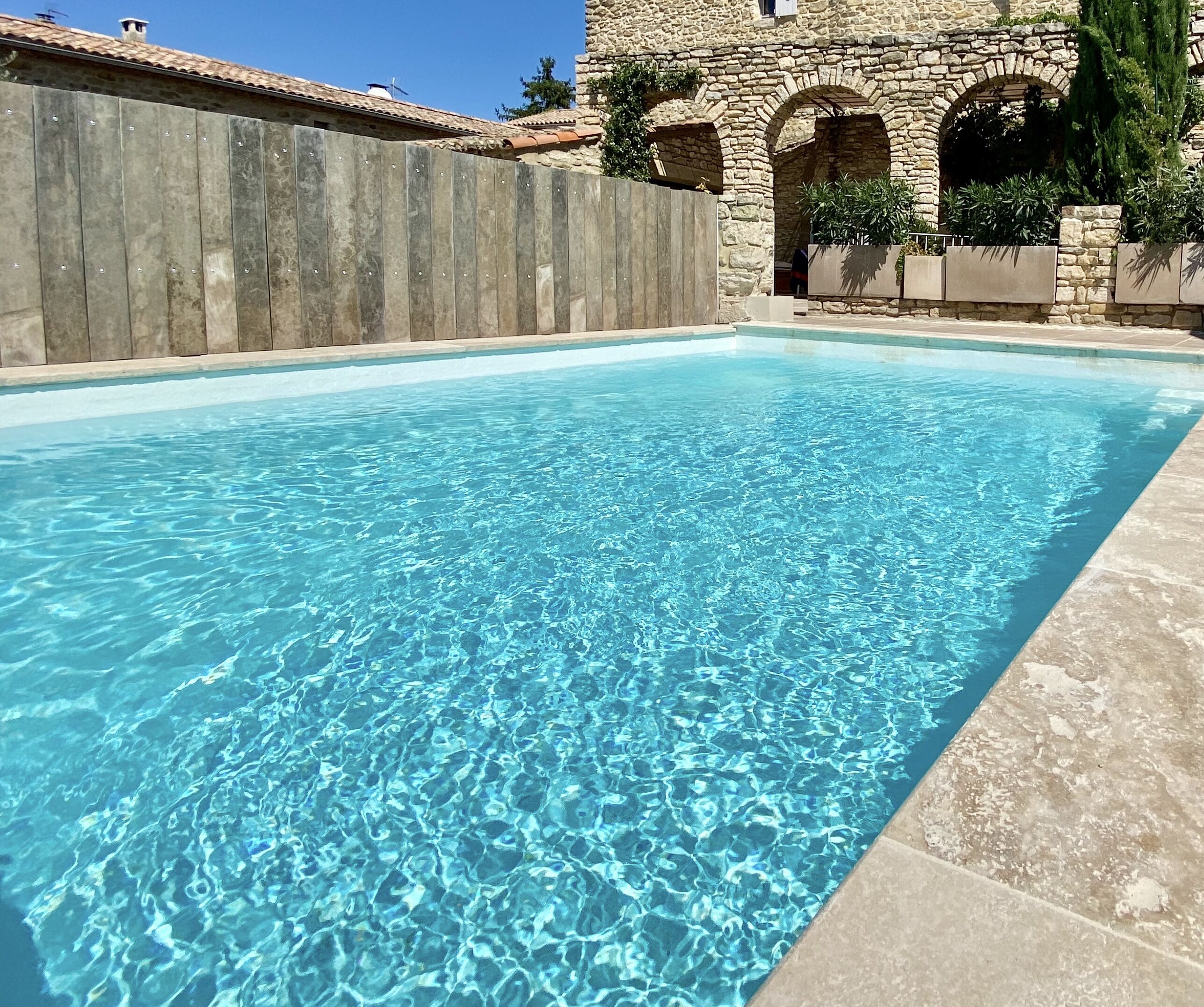 Une piscine aux eaux cristallines, bordée de murs en pierre et dotée d’ouvertures en arc de cercle.