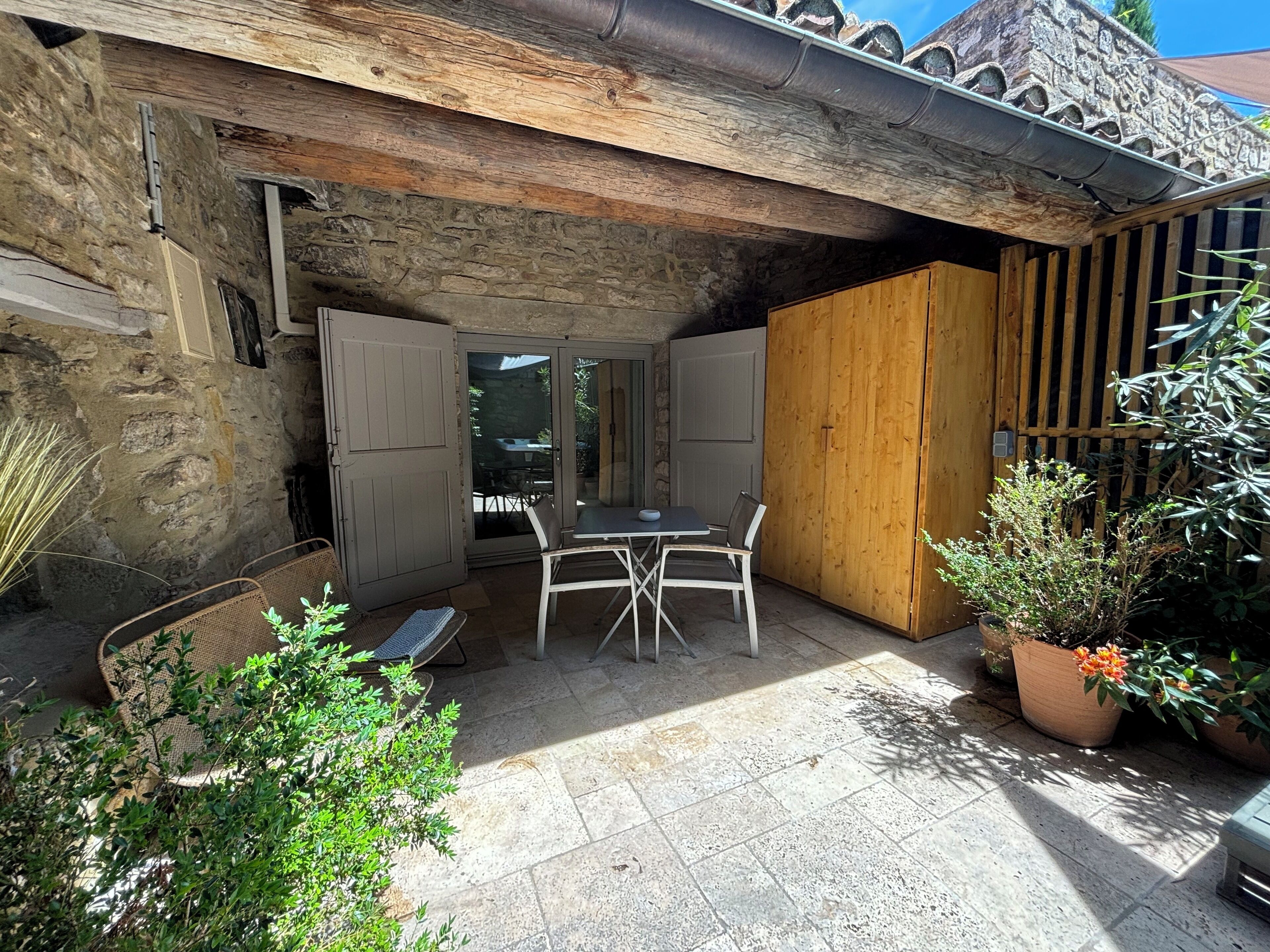 A stone building with a wooden door, a table with chairs, and potted plants.