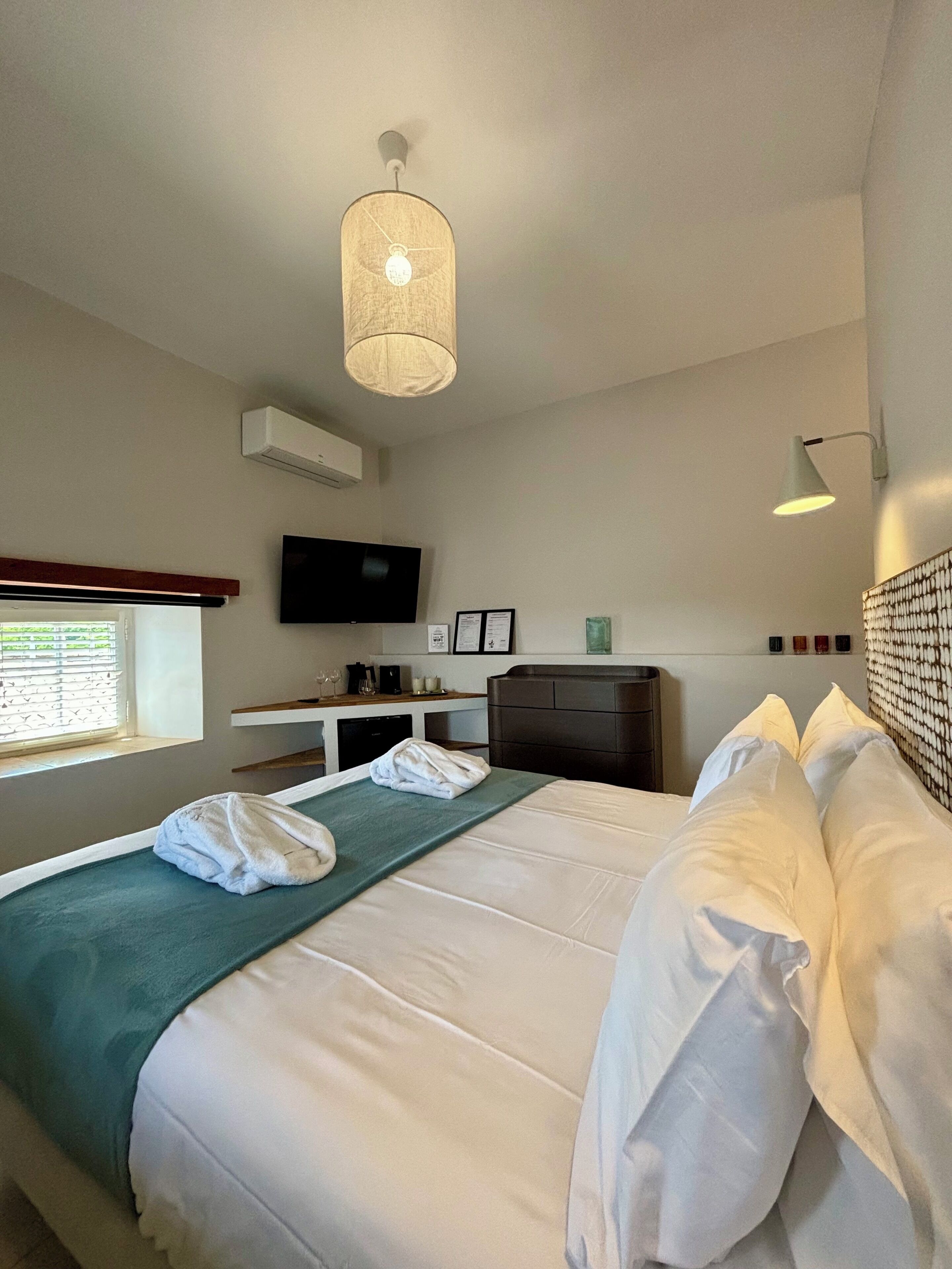 Quarto de hotel com uma cama, uma mesa, uma televisão e uma janela.