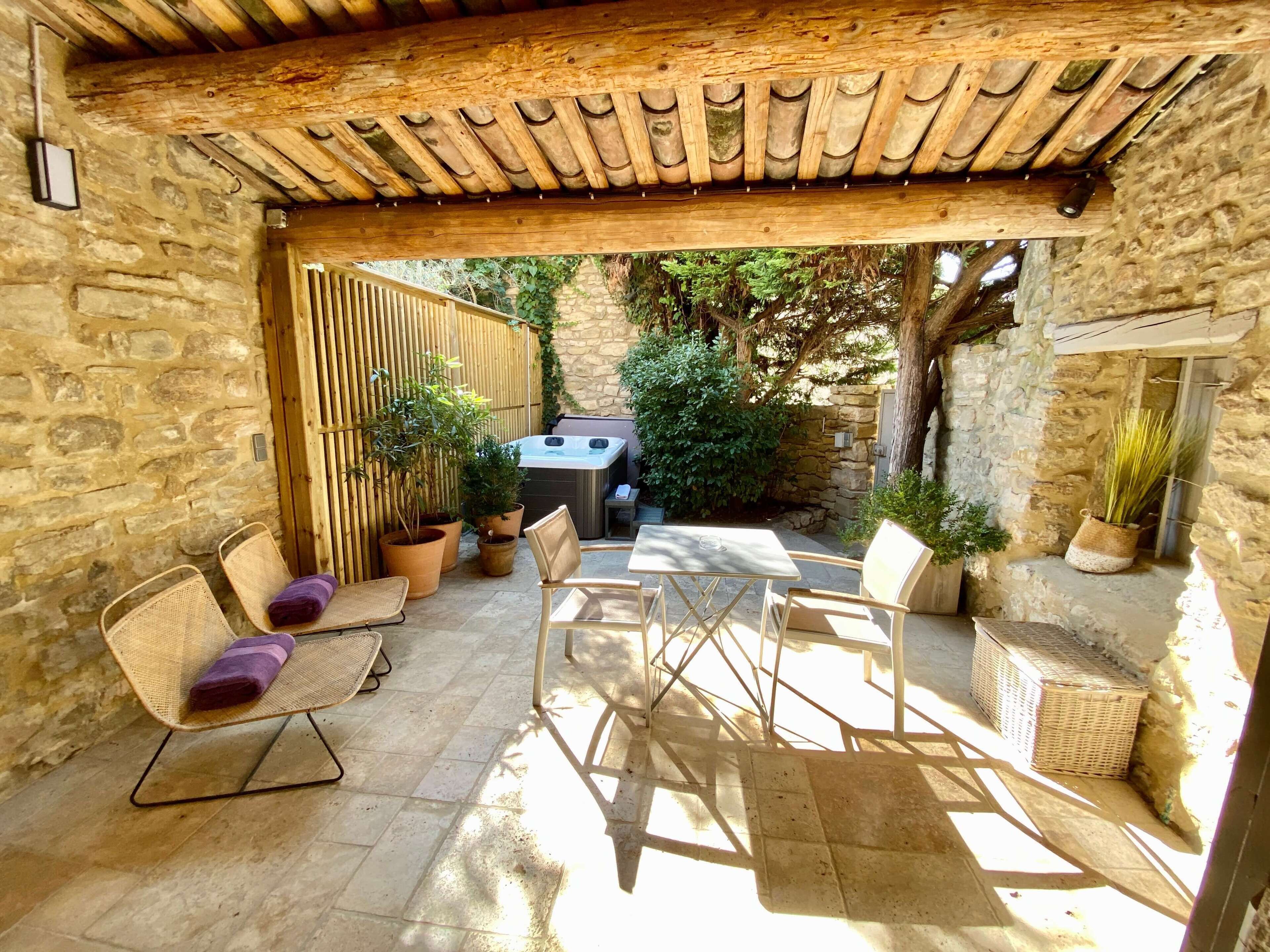 Un patio al aire libre con muros de piedra, una pérgola de madera, mobiliario de mimbre y plantas en macetas.