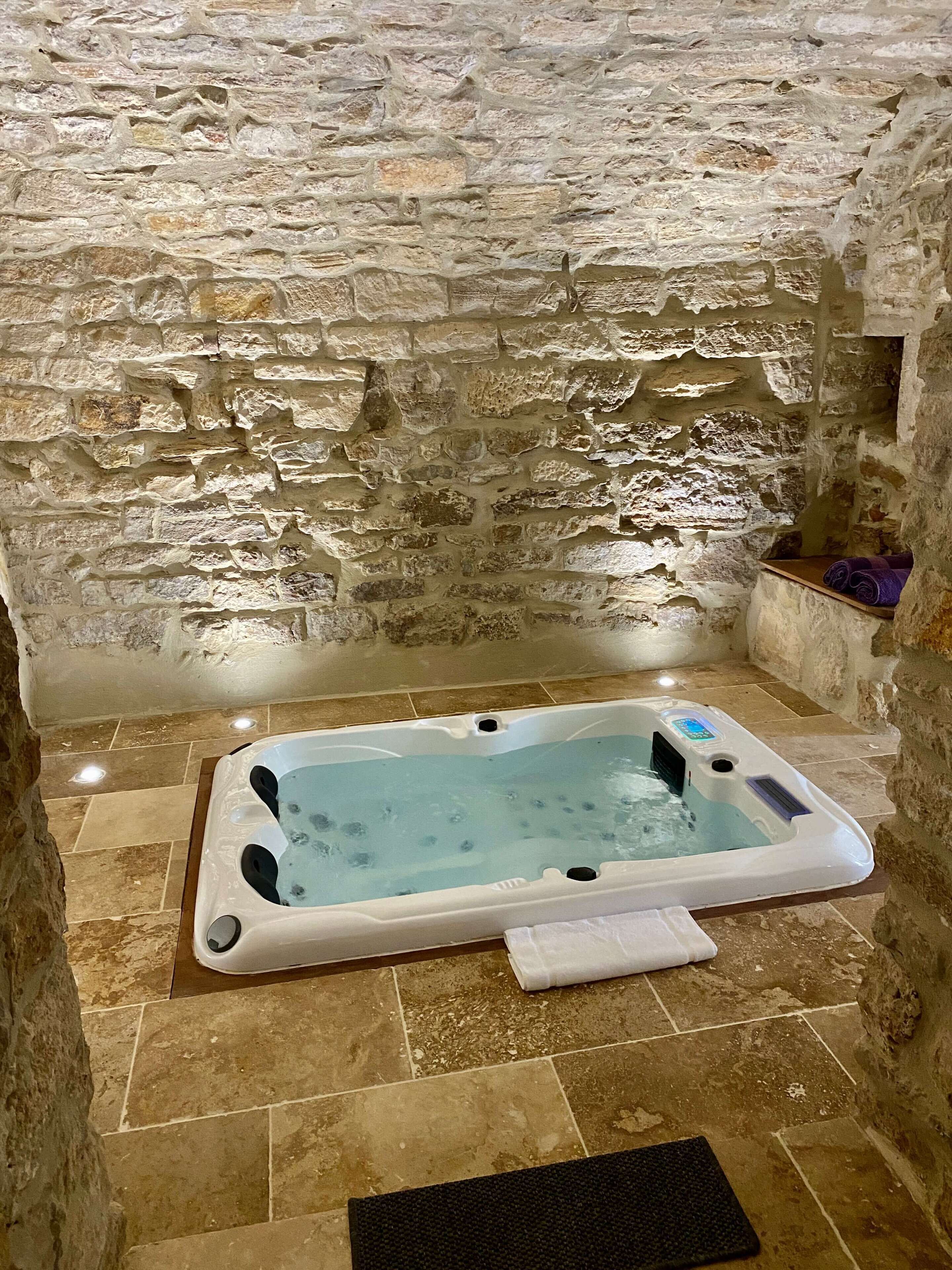 Een badkamer met stenen muren en een rechthoekig hottub.