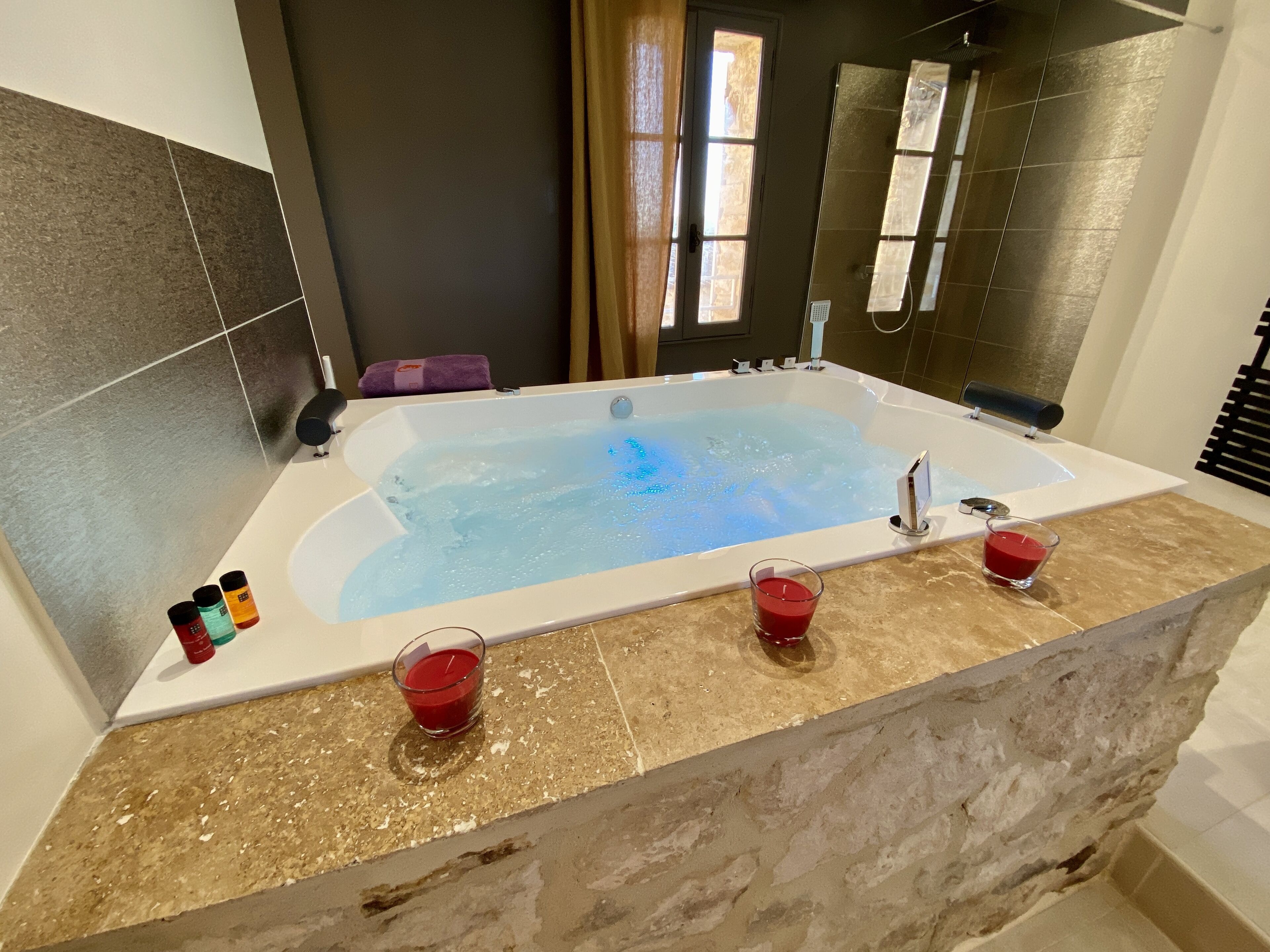 Un baño moderno con una bañera grande, una copa de líquido rojo y un juego de artículos de aseo en la encimera.