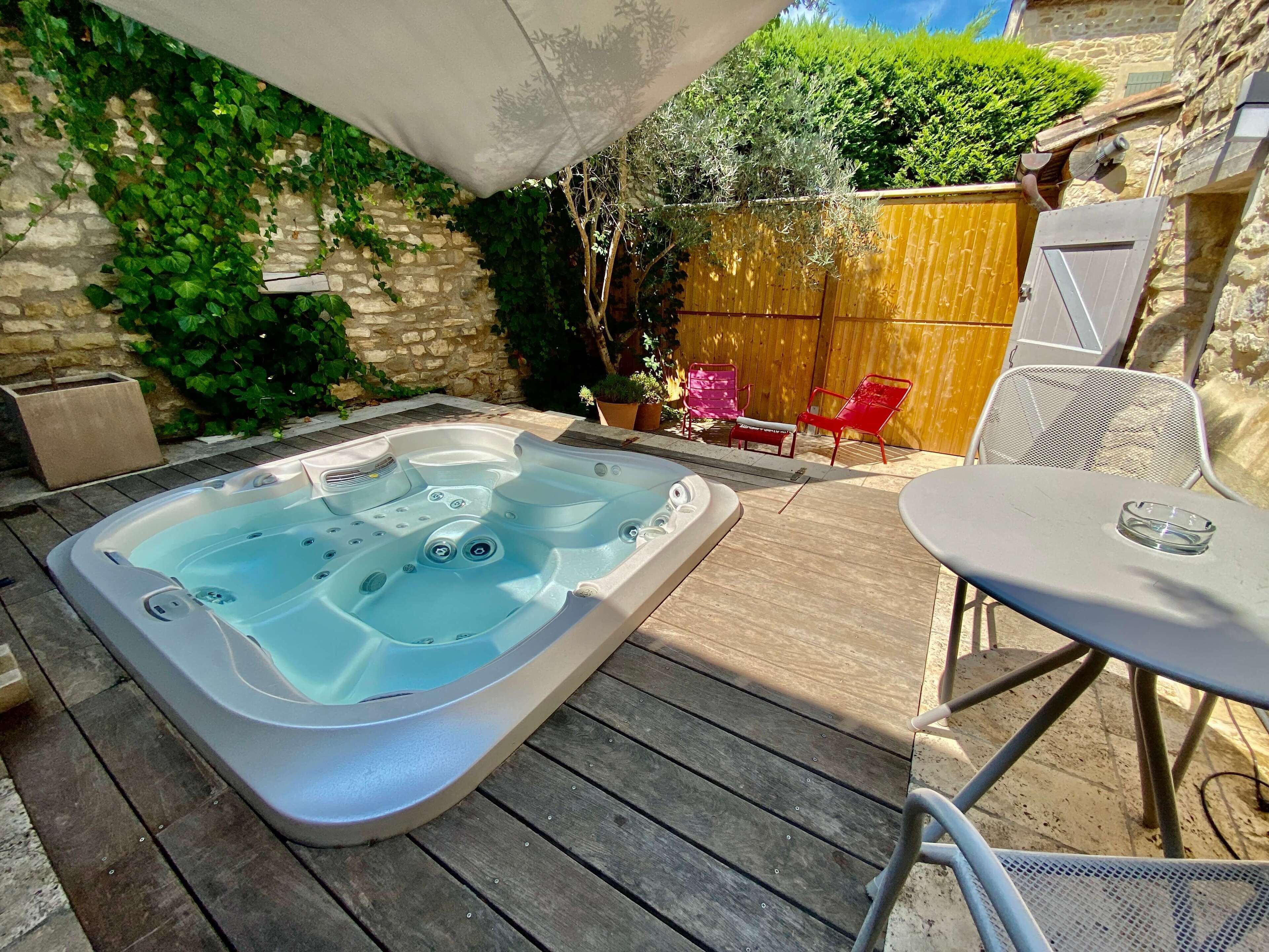 A hot tub on a wooden deck with a stone wall and greenery in the background.