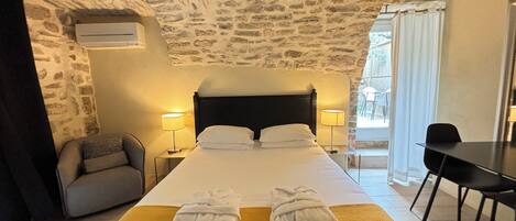 A hotel room with a stone ceiling, a bed with two towels, a desk, and a chair.