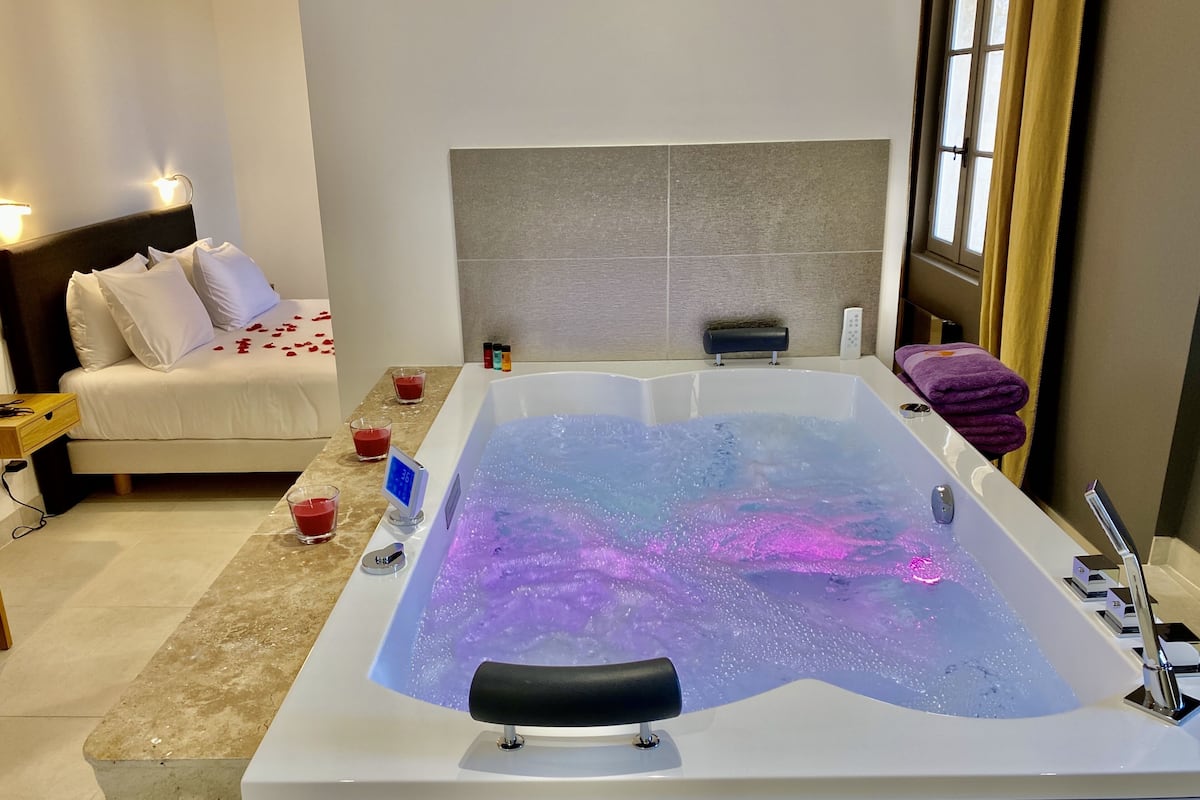 Ein modernes Badezimmer mit einer großen Badewanne, einem Nachttisch mit Lampe und einem kleinen Nachttisch mit Telefon.