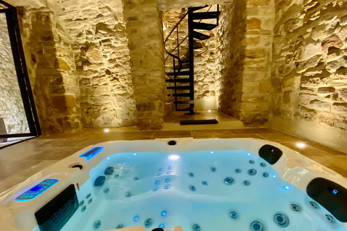 Ein Whirlpool in einem Raum mit Steinwänden, einer Holzleiter und einer digitalen Steuerung.
