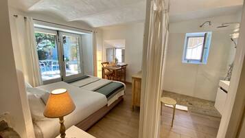 A bedroom with a bed, bedside lamp, and a view of the outside. There is a small table with a chair and a window.