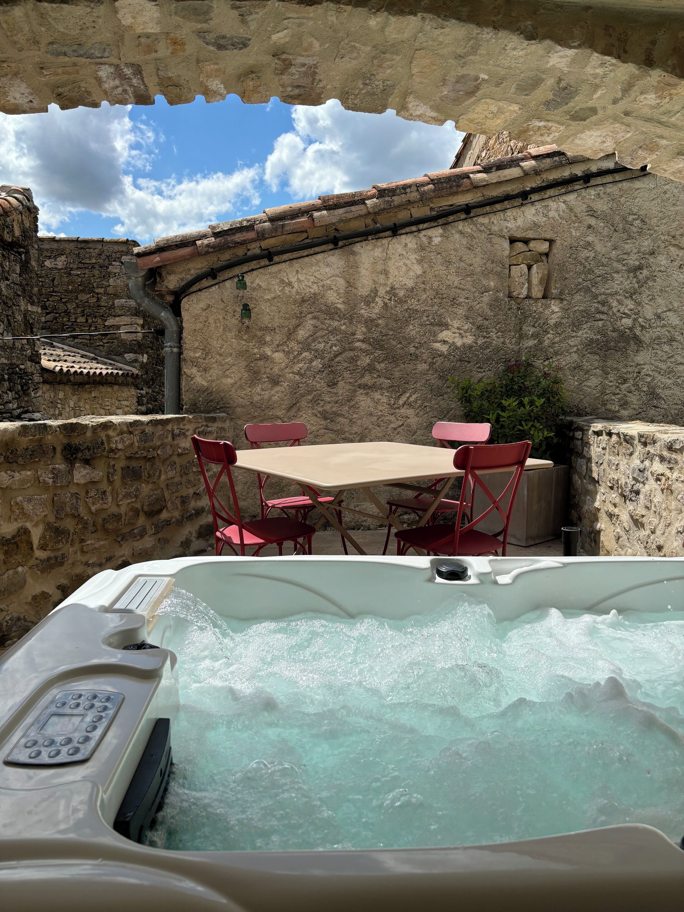 Un bain à remous avec une table et des chaises, installé à l’extérieur, dans un décor agrémenté de murs en pierre et sous un ciel dégagé.