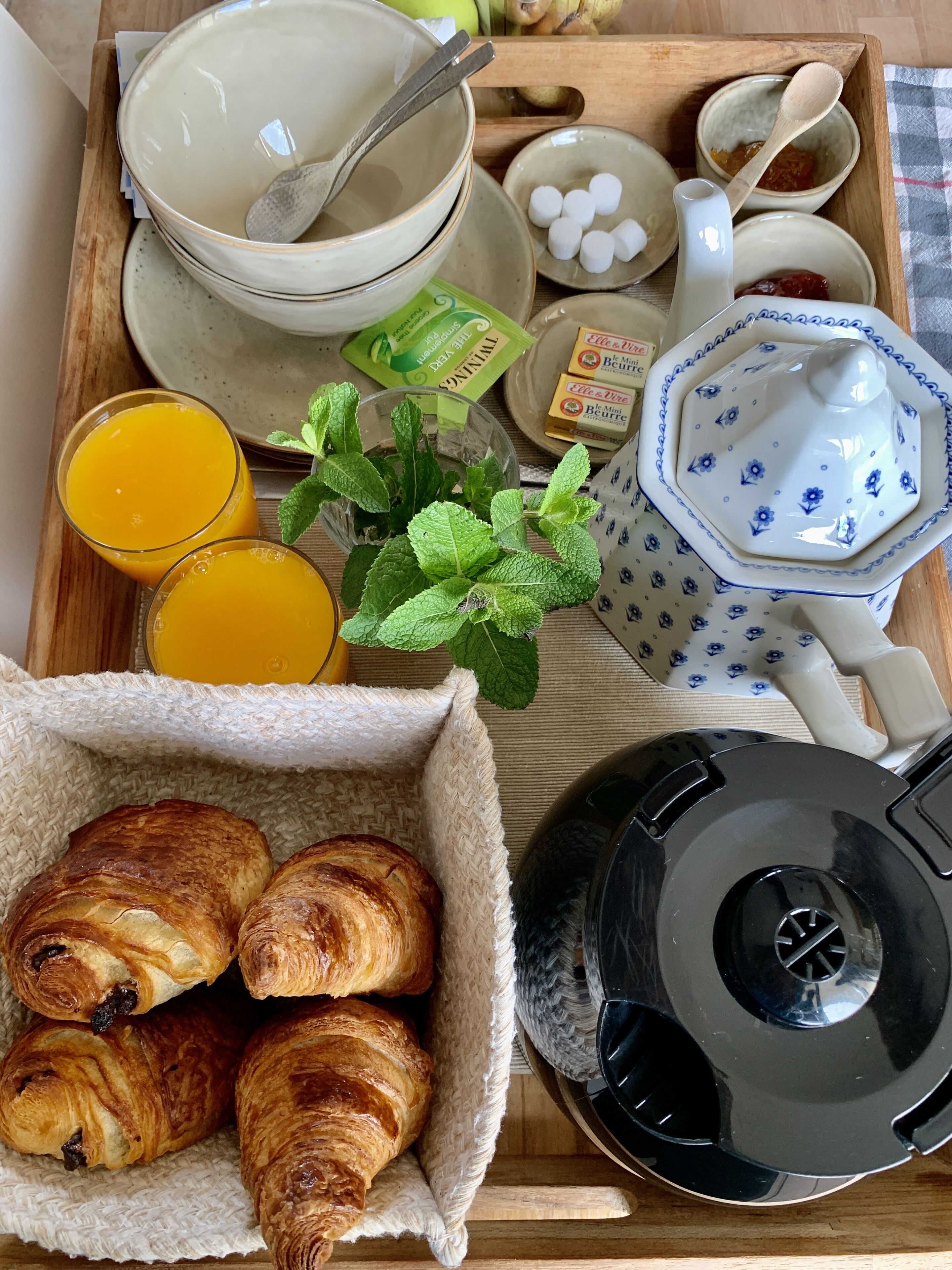 Una bandeja de desayuno con cruasanes, jugo de naranja, tetera y cafetera.