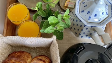Una bandeja de desayuno con cruasanes, jugo de naranja, tetera y cafetera.