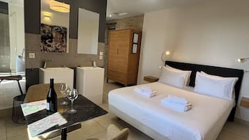 Ein Hotelzimmer mit einem Bett, einem Schreibtisch mit Stuhl, einem kleinen Tisch mit Flasche und Gläsern, einem Kleiderschrank und einem Spiegel.