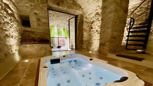 Un espace bien-être comprenant un jacuzzi, des murs en pierre et un escalier.
