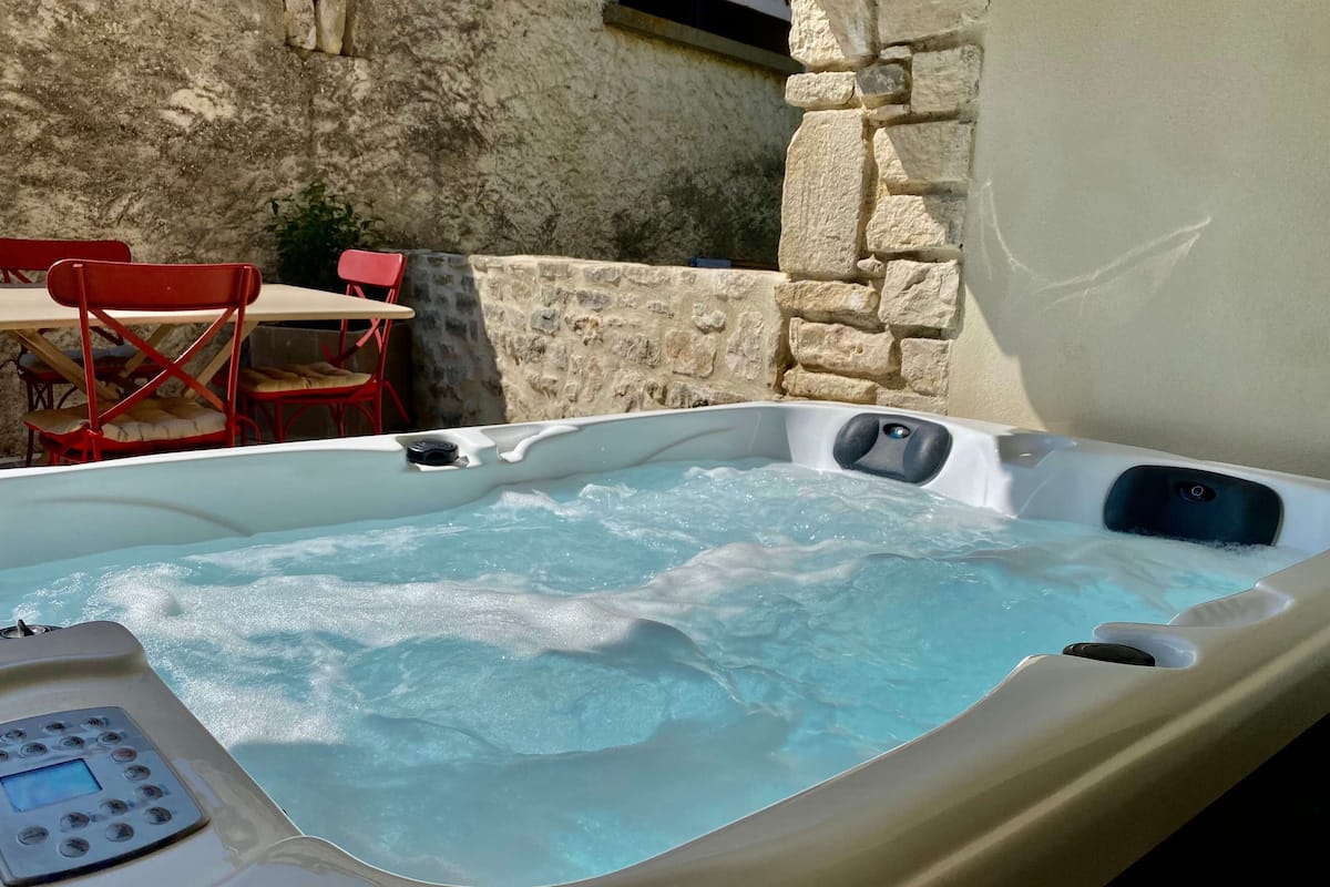 Ein Whirlpool mit Bedienfeld, umgeben von Steinmauern und roten Stühlen.
