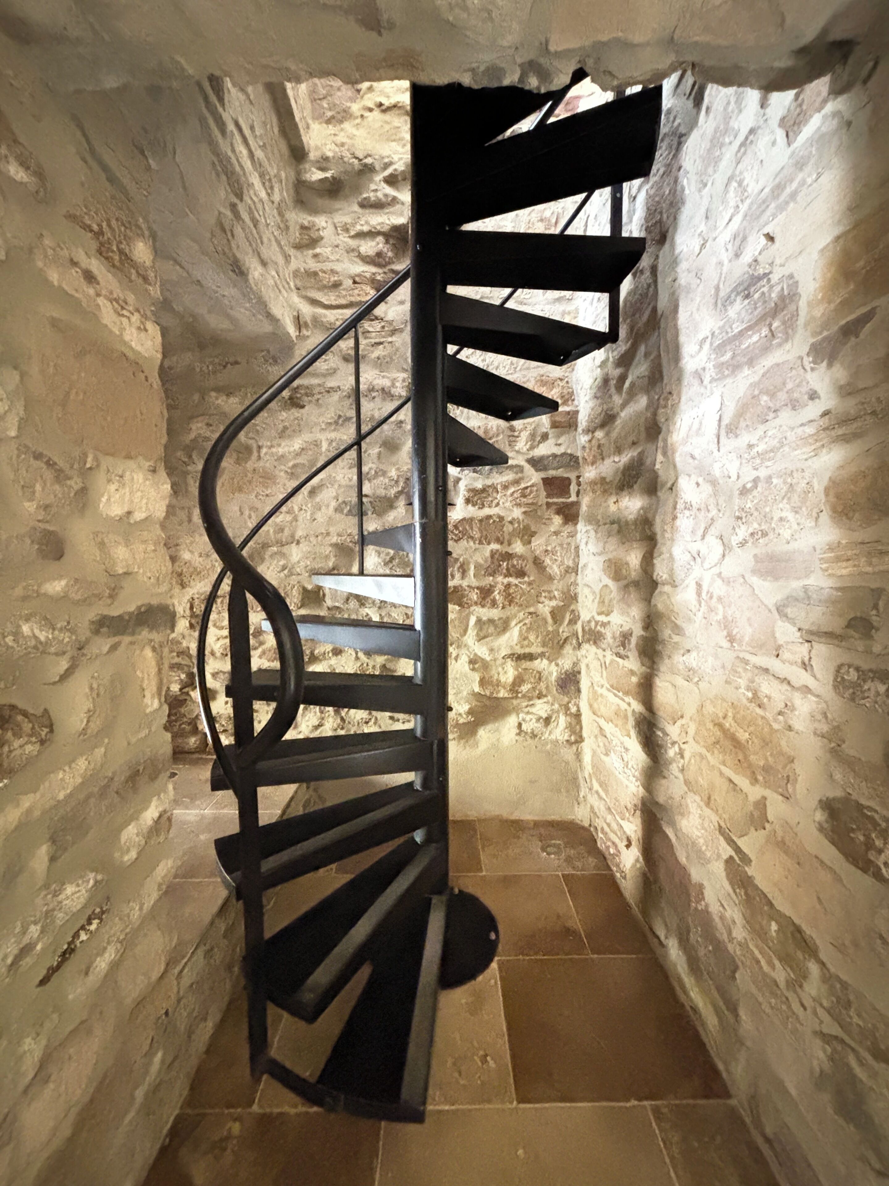 Una escalera de caracol con barandilla metálica en una habitación con paredes de piedra.