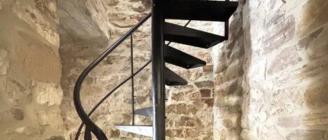 Una escalera de caracol con barandilla metálica en una habitación con paredes de piedra.