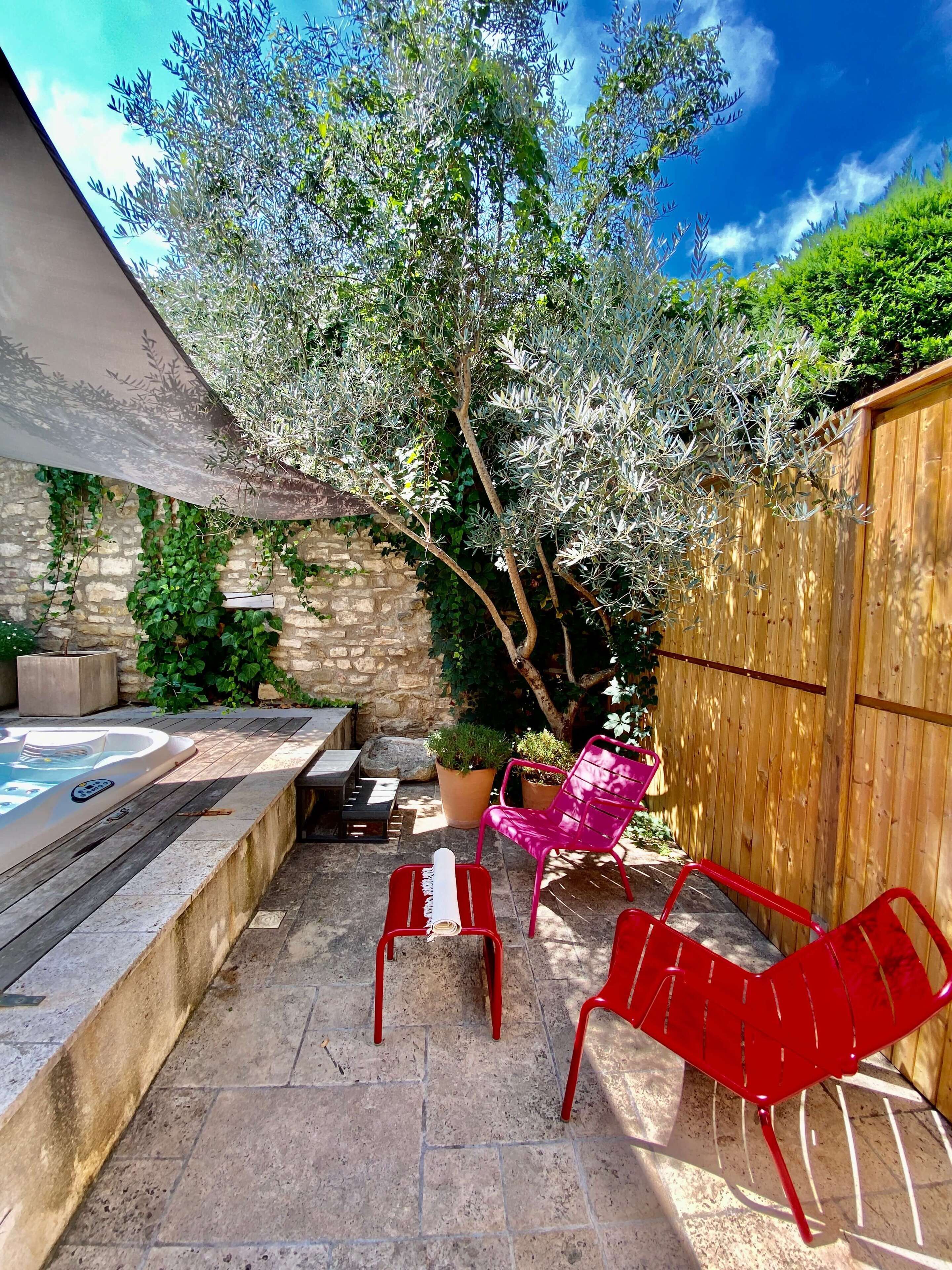 A patio with a hot tub, red chairs, and a wooden fence.