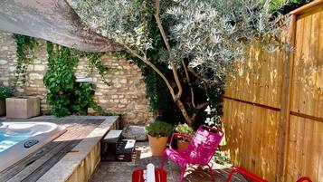 A patio with a hot tub, red chairs, and a wooden fence.