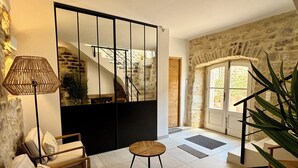 Un salon moderne avec un canapé, une table basse et une lampe. Un escalier mène à un niveau supérieur. La pièce est dotée de murs en pierre et d’un grand miroir.