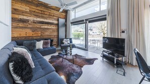 Un saló modern amb una paret de fusta, una finestra gran, un sofà, un televisor i una zona de menjador.