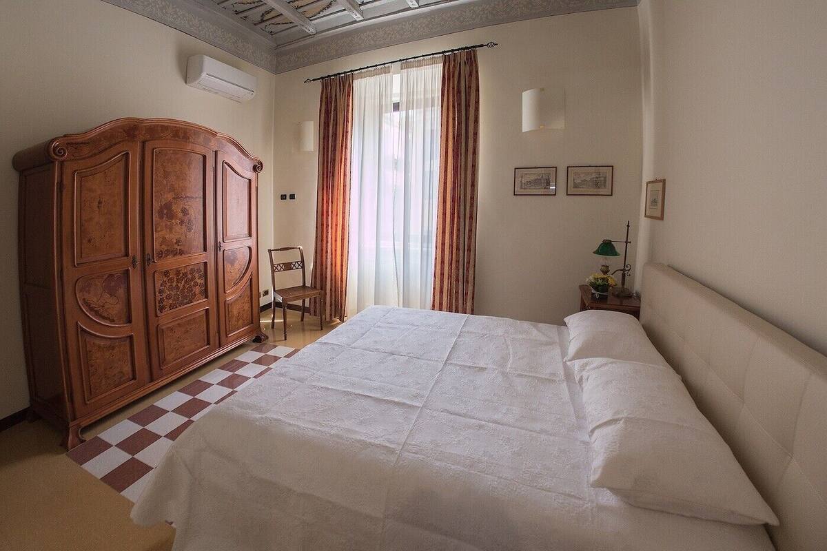 A bedroom with a large bed, a wooden wardrobe, a chair, and a checkered floor.