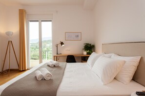A hotel room with a bed, a desk, a chair, a lamp, a plant, and a view of the outdoors.