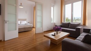 Ein modernes Wohnzimmer mit Sofa, Couchtisch mit Vase, Bett mit Kopfteil und großen Fenstern mit Vorhängen.