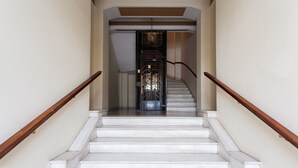 Eine Treppe mit weißen Stufen und Holzhandläufen, die zu einer Tür mit einem Metallgitter führt.