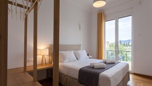 Ein Schlafzimmer mit Bett, Nachttisch, Lampe und Blick ins Freie durch ein großes Fenster.