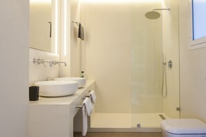 A modern bathroom with two sinks, a glass-enclosed shower, and a toilet.