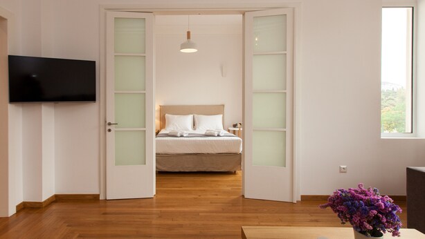 Ein Schlafzimmer mit einem Bett, einem an der Wand montierten Fernseher und einem Fenster mit Blick ins Grüne.