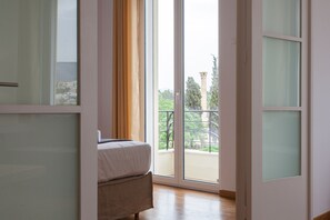 A bedroom with a bed, a window, and a view of a balcony.