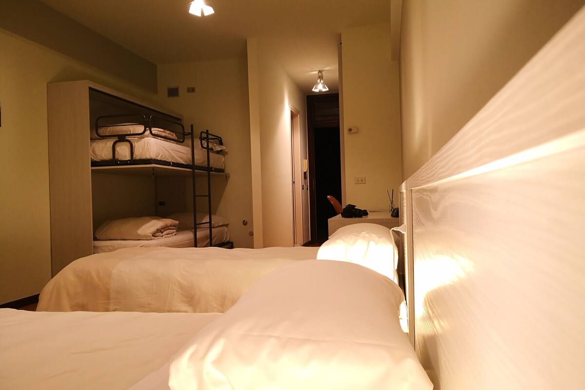 Una habitación de hotel con dos camas, una litera y un escritorio con una silla.