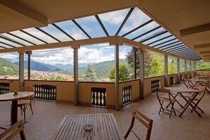 A covered outdoor seating area with tables and chairs, overlooking a mountainous landscape. - Grem Bike Hostel (Premolo)