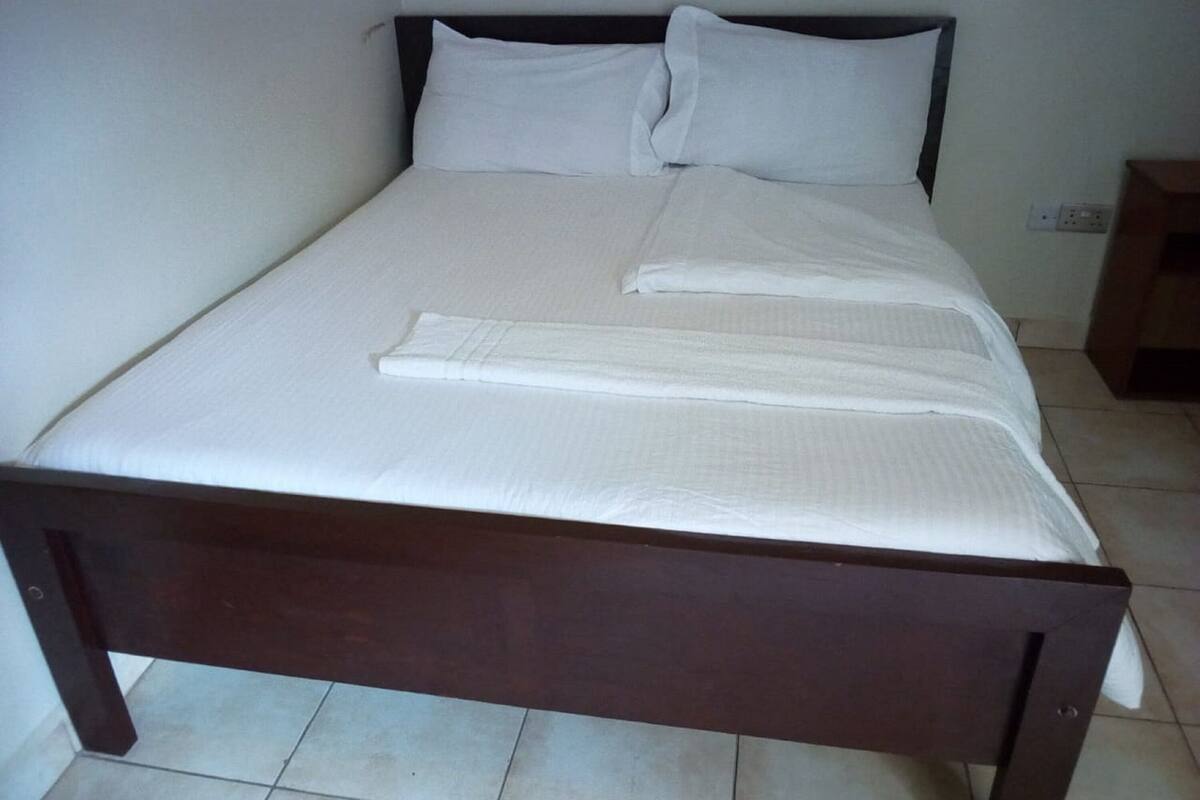 A single bed with white linens and pillows, a wooden frame, and a tiled floor.