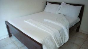 A single bed with a wooden frame and white bedding in a room with plain walls and tiled flooring.