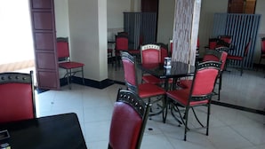 A dining area with red upholstered chairs and a glass table. There is a door on the left and a partition with vertical blinds in the background.