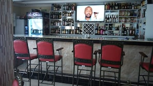 A bar area with a television screen, multiple liquor bottles, and red bar stools.
