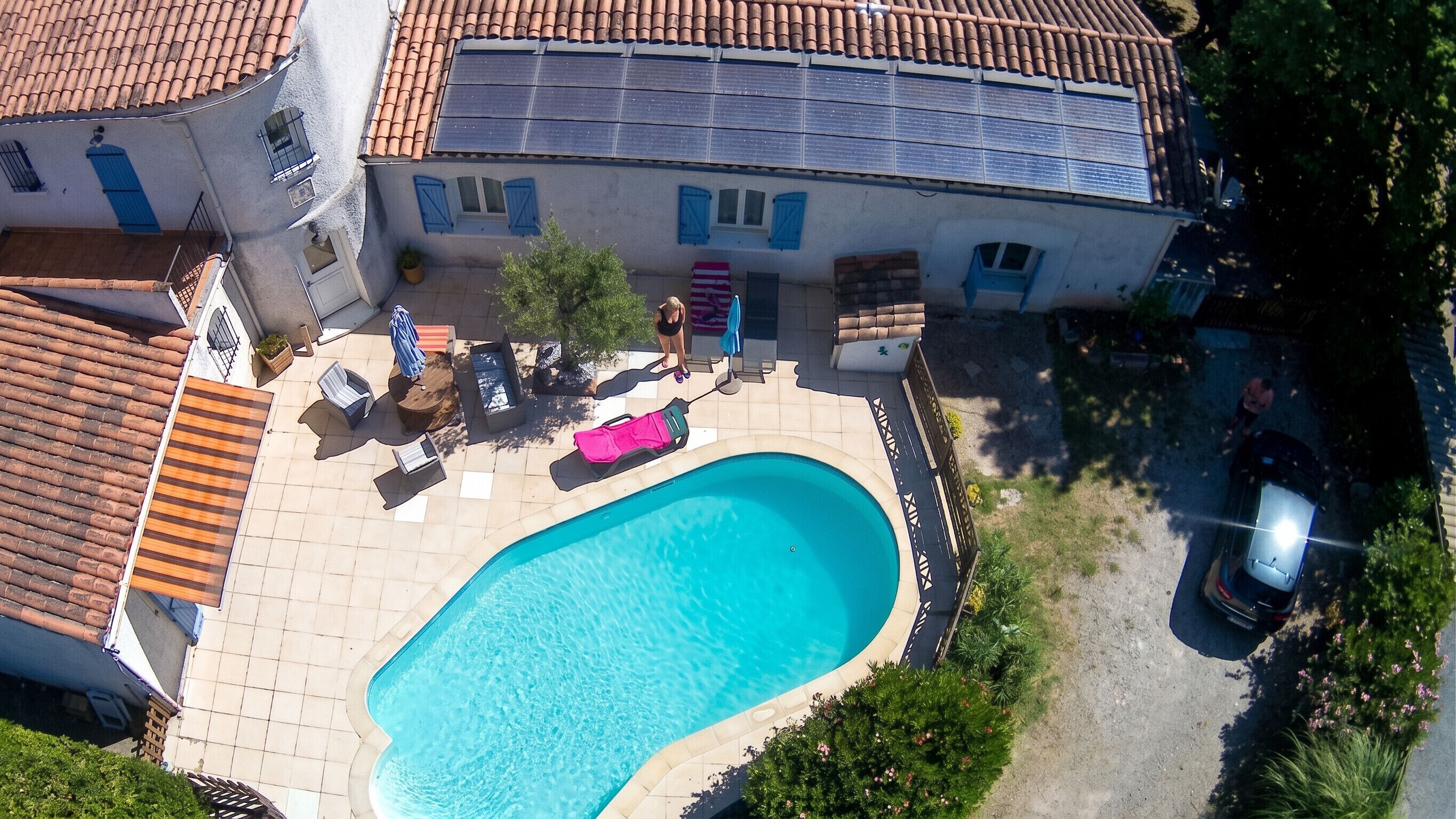 A residential property with a swimming pool, tiled patio, and a large house with a tiled roof.