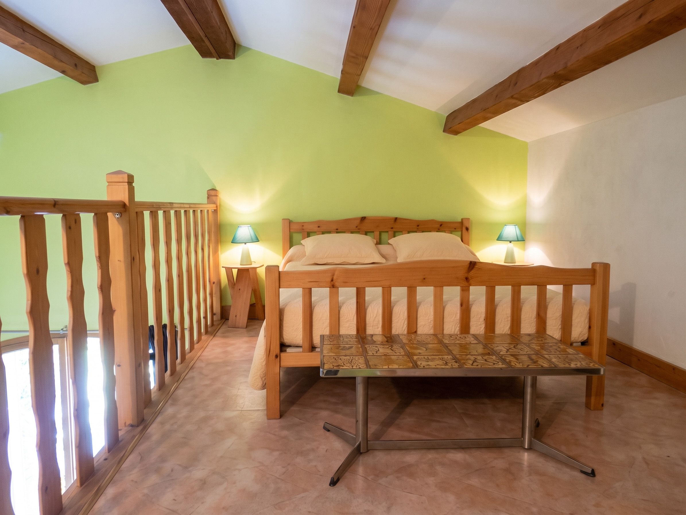Une chambre à coucher avec un lit en bois, deux lampes de chevet, un banc en bois et un balcon doté d’une balustrade en bois.