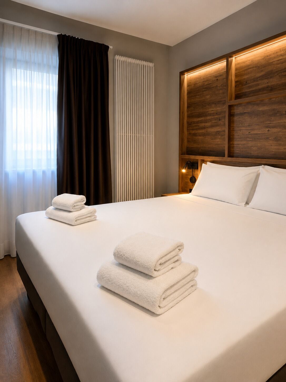 A hotel room with a large bed, a radiator, and a wooden headboard.