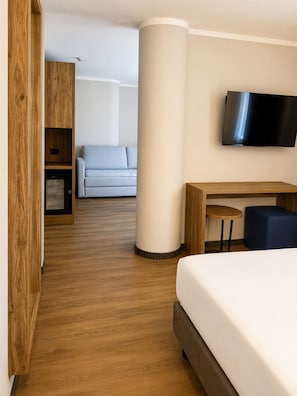 A hotel room with a bed, a desk, a television, a sofa, and a wooden wardrobe.