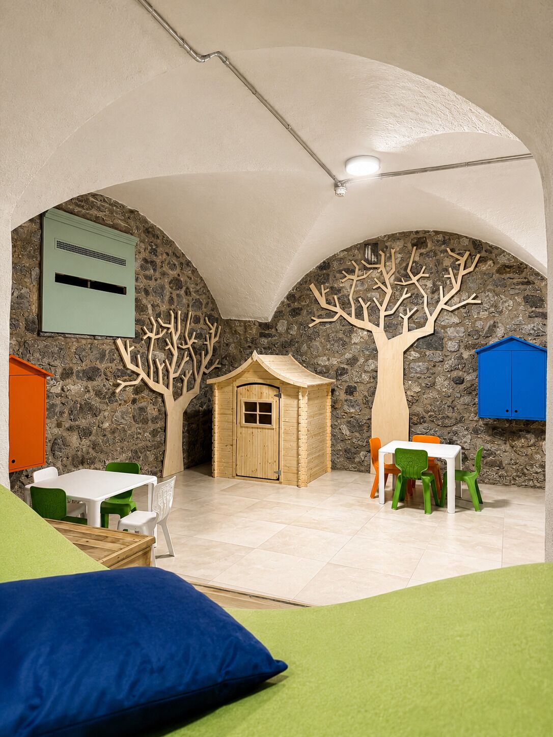 Een kinderspeelruimte met een stenen muur, een houten speelhuisje en een tafel met stoelen.