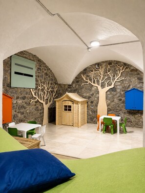 A children's playroom with a stone wall, a wooden playhouse, and a table with chairs. - Parc Hotel Posta (Marebbe)